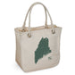 A beige organic cotton Maine Rope Tote from Rustic County with sturdy rope handles and a green brushstroke map of Maine imprinted on one side, along with the initials "RC" in a lower corner.